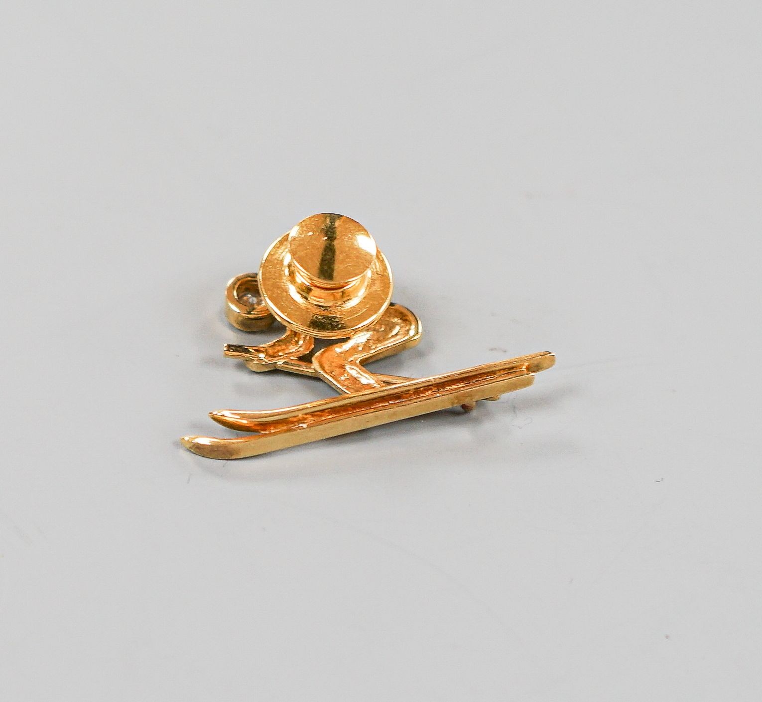 A yellow metal and single stone diamond set dress stud?, modelled as a skier, 31mm, gross 4.5 grams.